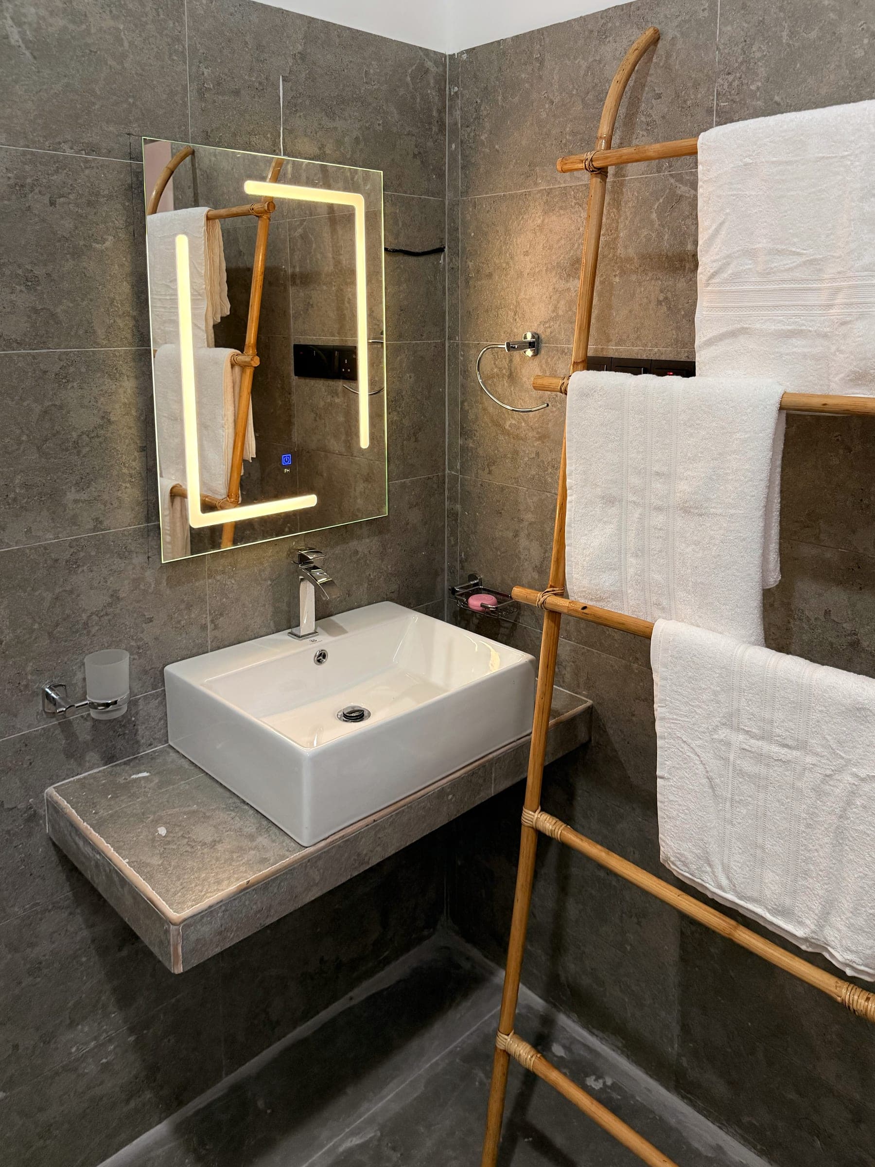 Basin on a stone shelf with a backlit mirror and a bamboo towel ladder