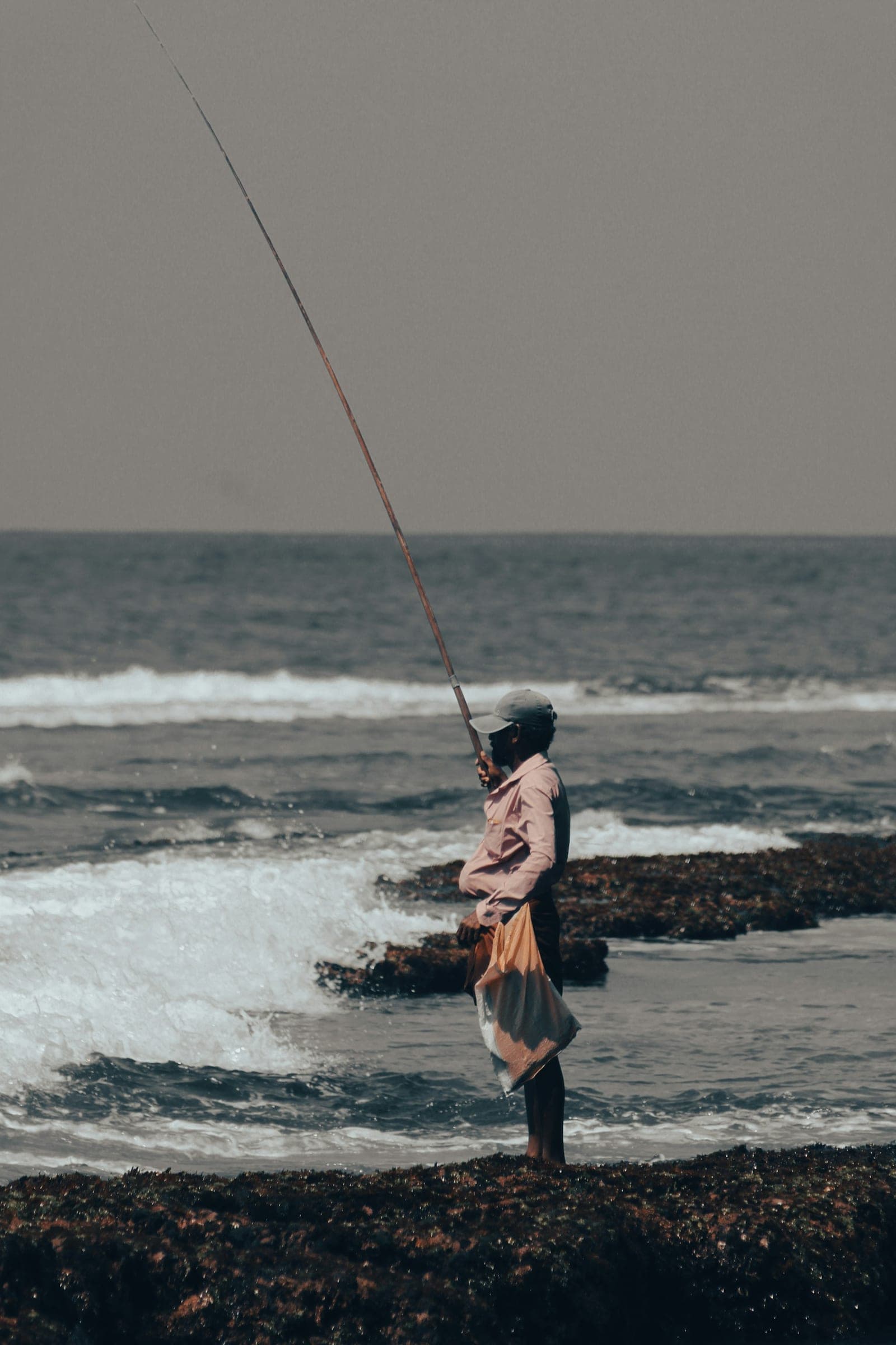 Fisherman with a long rod standing on rocks in the surf