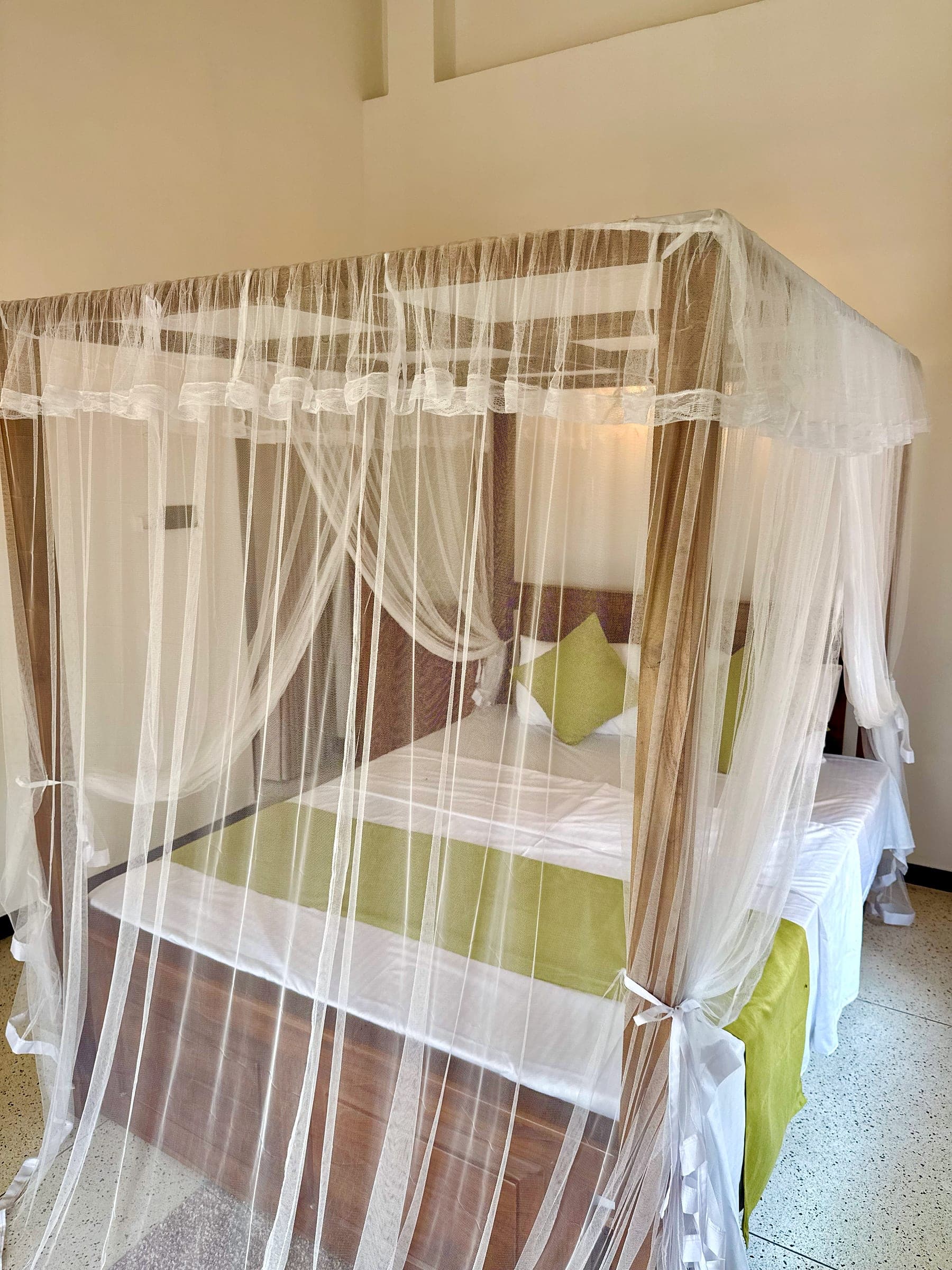Canopy king bed enclosed in a white mosquito net, with lime-green cushions and runner