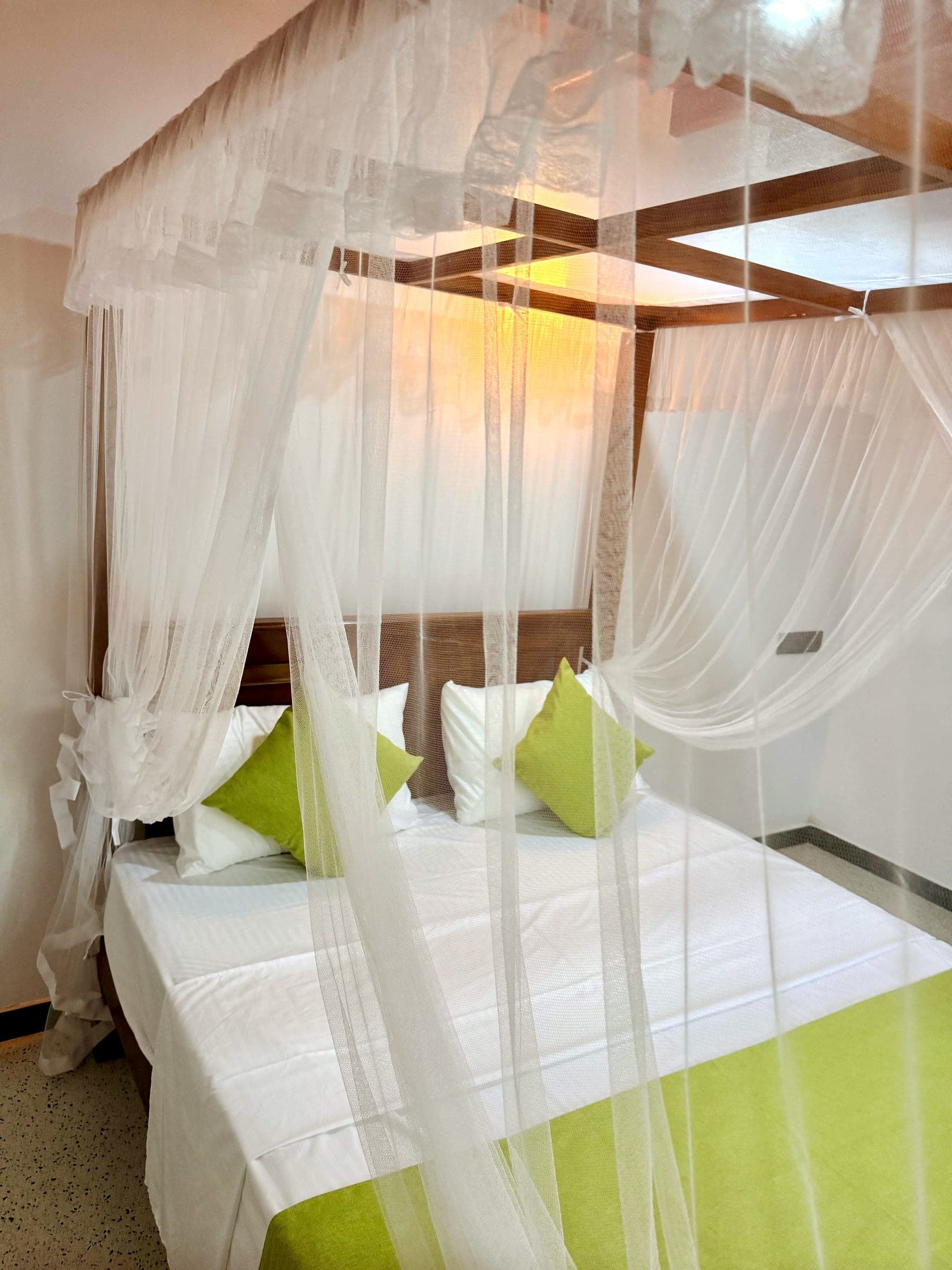 Looking through the white mosquito net to a canopy king bed, its lime-green cushions and runner