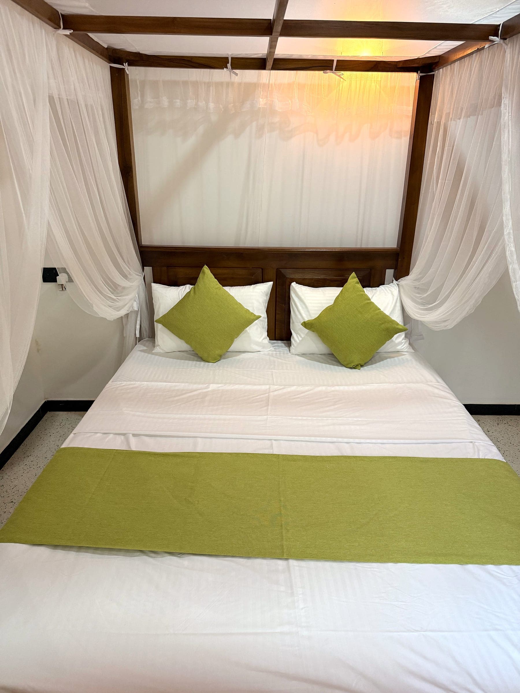 Canopy king bed with the mosquito net tied back at each post, lime-green cushions and runner