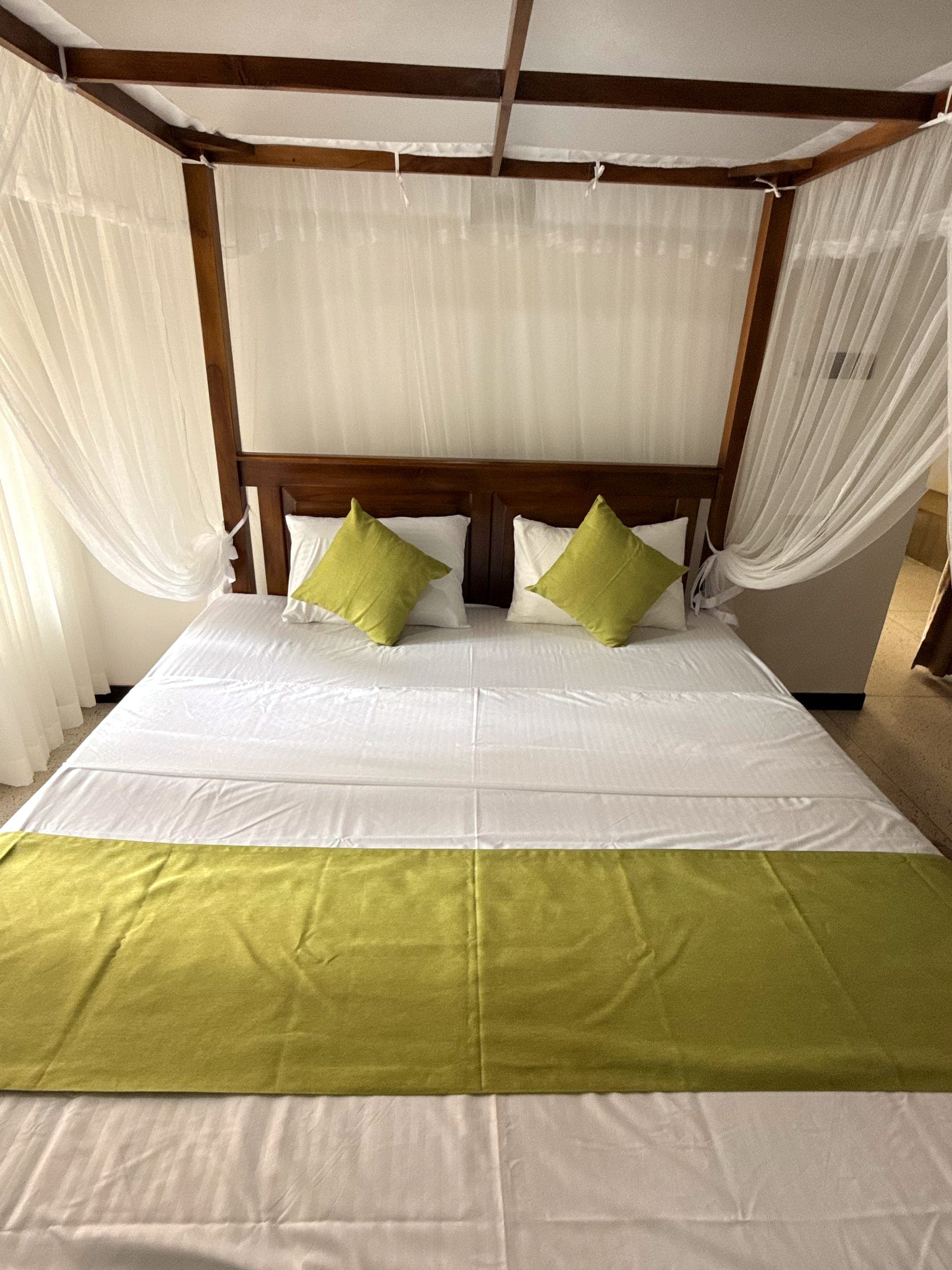 Canopy king bed with lime-green cushions and runner, seen from the foot of the bed