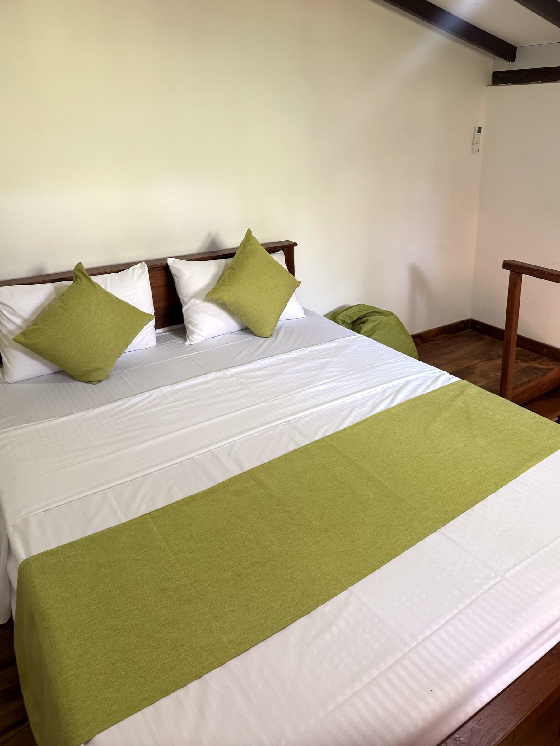Queen bed in the loft with lime-green cushions and runner, beside the teak stair rail