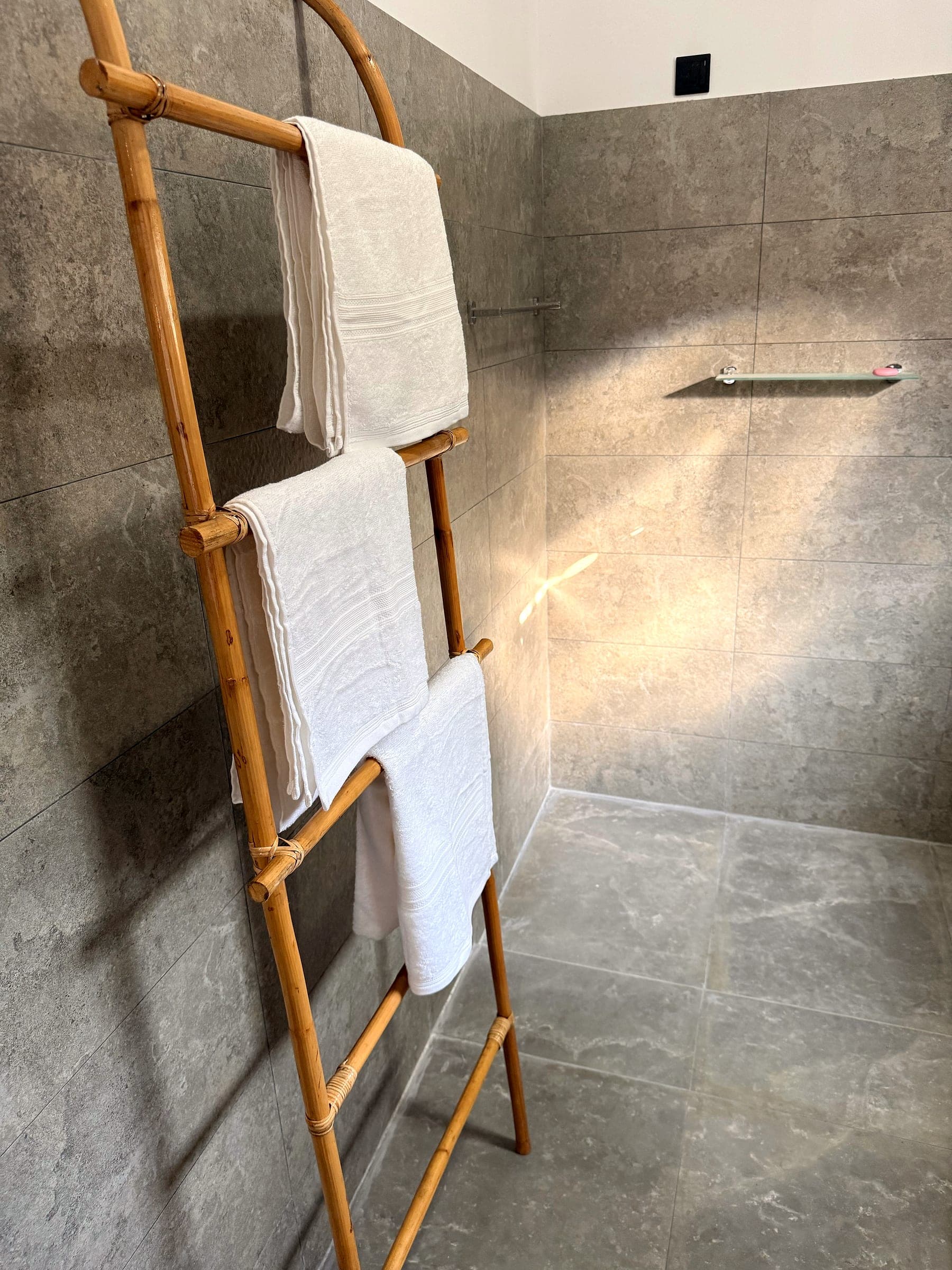 Bamboo ladder hung with white towels against the grey stone tiles of the shower