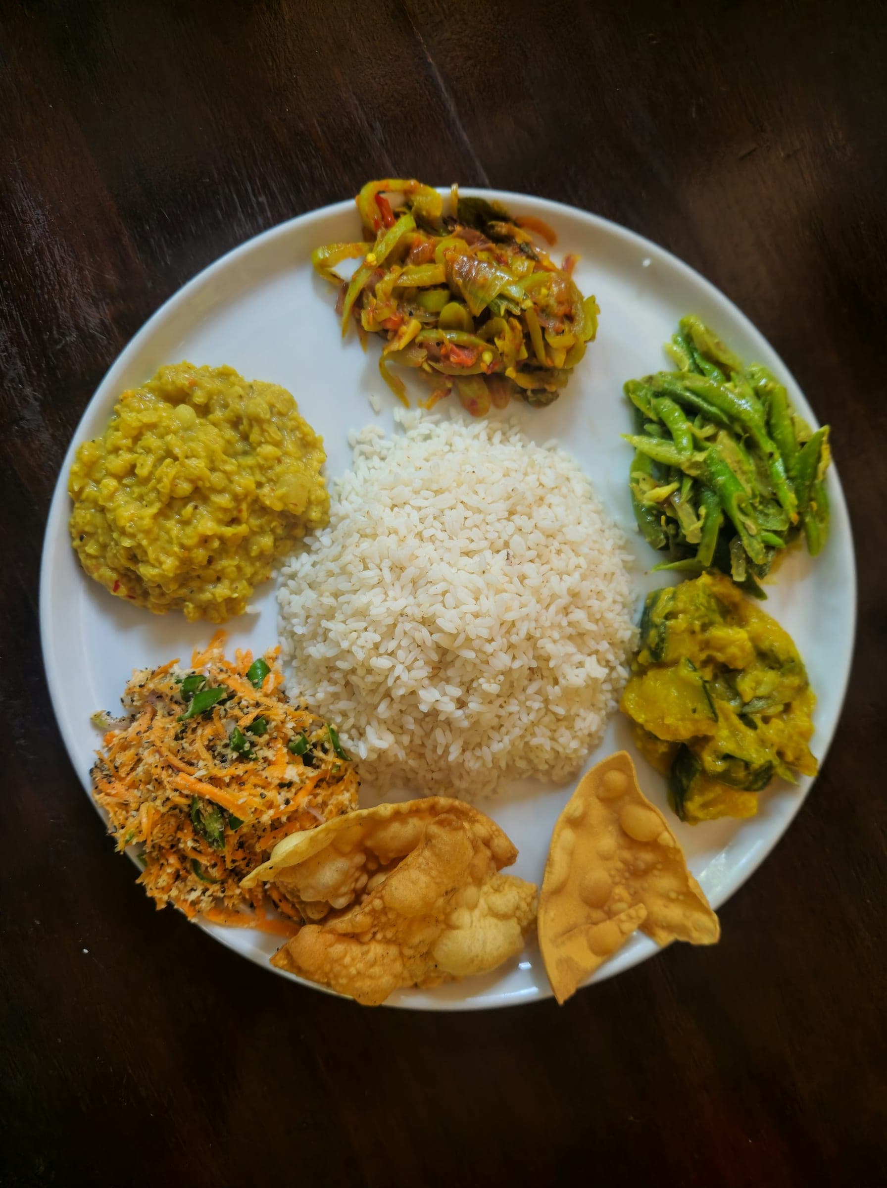 Plate of rice and curry with dhal, green beans and papadums